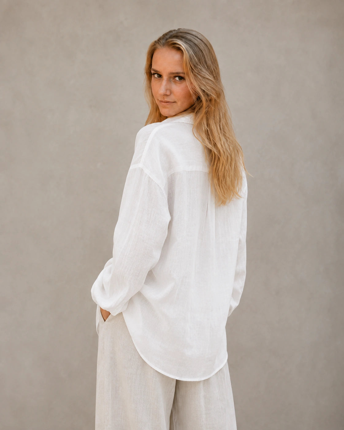 Driekwart achteraanzicht van een vrouw in een oversized wolkenwit linnen blouse.