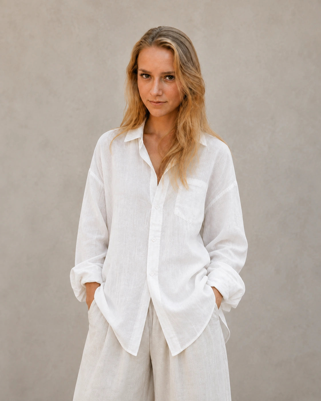 Vrouw draagt een oversized wolkenwit linnen blouse met reverskraag, handen in zakken, vooraanzicht.