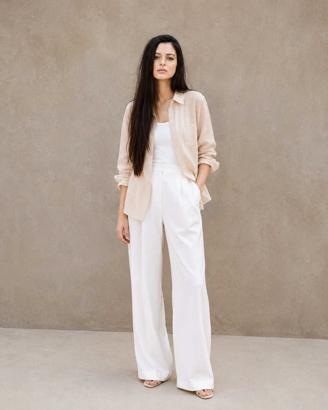 Full-length shot of a woman wearing an open beige lyocell-linen shirt, styled with wide-leg white trousers.