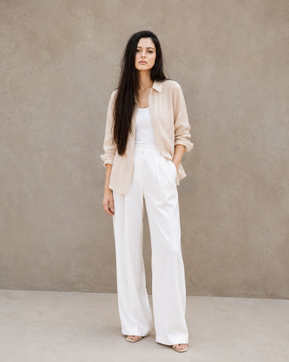 Full-length shot of a woman wearing an open beige lyocell-linen shirt, styled with wide-leg white trousers.