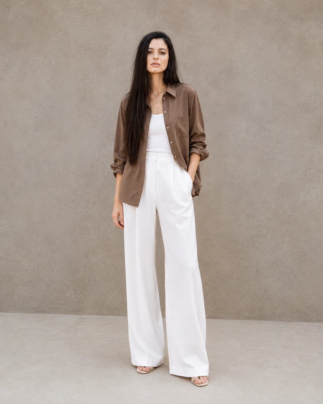 Full-length shot of a woman wearing an open brown lyocell-linen shirt, styled with wide-leg white trousers.
