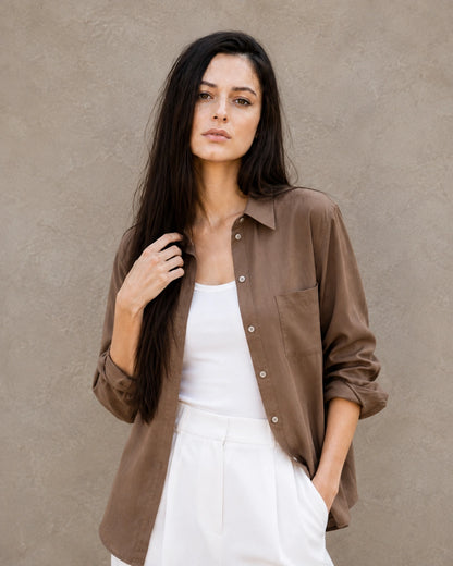 Woman wearing an open, cardigan-style brown lyocell-linen shirt with a patch pocket, over a white top.