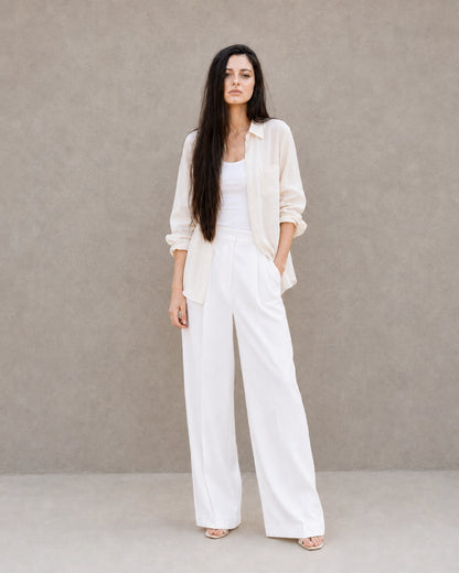 Full-length shot of a woman wearing an open off-white lyocell-linen shirt, styled with wide-leg white trousers.