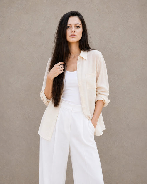 Woman wearing an open, cardigan-style off-white lyocell-linen shirt with a patch pocket, over a white top.
