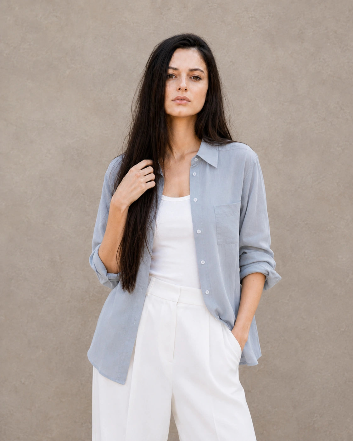 Woman wearing an open, cardigan-style grey-blue lyocell-linen shirt with a patch pocket, over a white top.