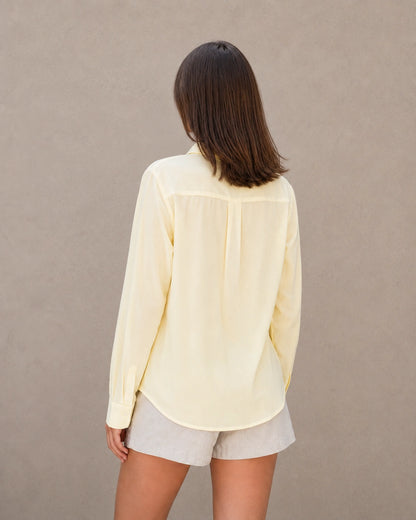 Achteraanzicht van een geel tencel-linnen doorknoopblouse met lange mouwen.