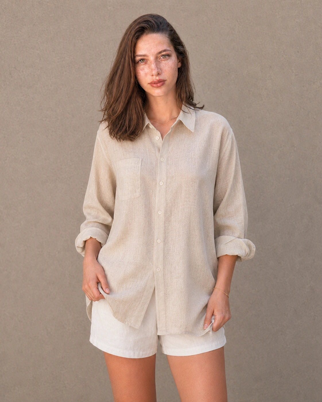 Volledige look van een vrouw in een lang naturel linnen-katoenen blousejasje, gecombineerd met een witte short.