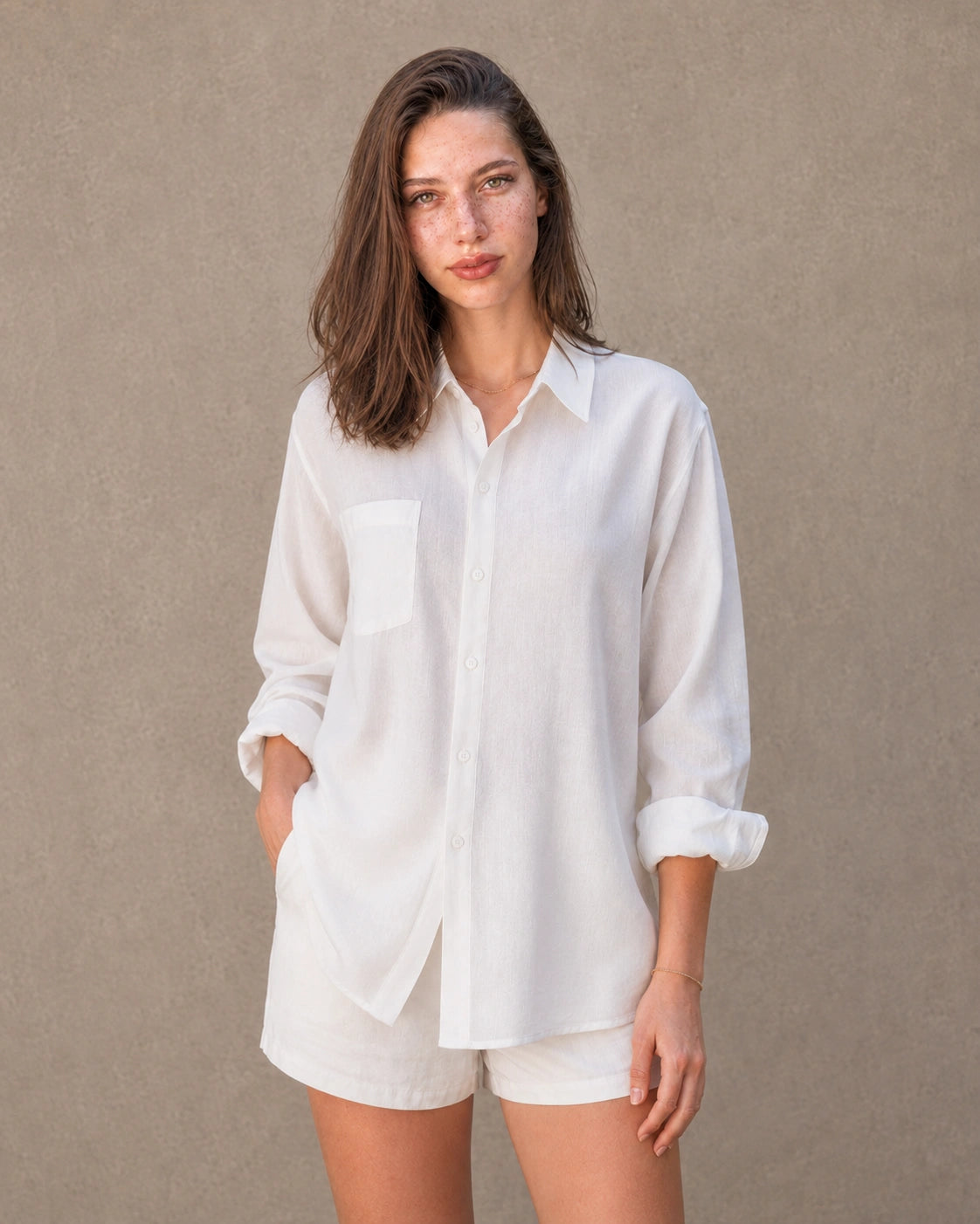 Volledige look van een vrouw in een lang wit linnen-katoenen blousejasje, gecombineerd met een witte short.