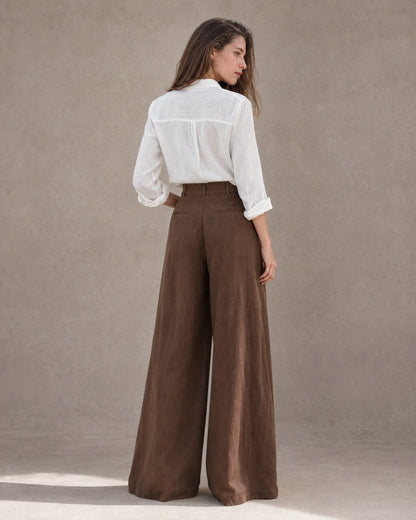 Achteraanzicht van model in een wijde broek dames in bruine katoen-linnenmix met hoge taille en wit linnen overhemd.