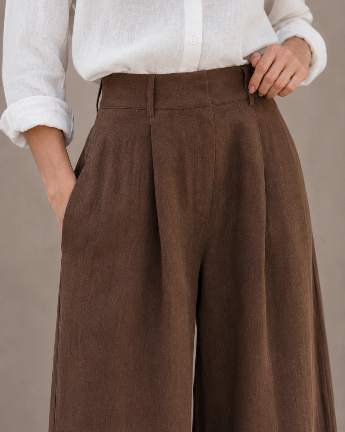 Close-up van de hoge, geplooide taille en voorzak van een wijde broek dames in bruine katoen-linnenmix.