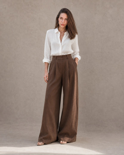Model in een wijde broek dames in bruine katoen-linnenmix met een hand in de zak, vooraanzicht, met zicht op de vloeiende wijde pijp.