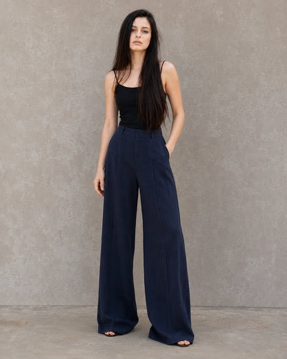 Model draagt een marineblauwe wijde broek dames in katoen-linnenmix met geplooide hoge taille, gestyled met een zwart hemdje, vooraanzicht.