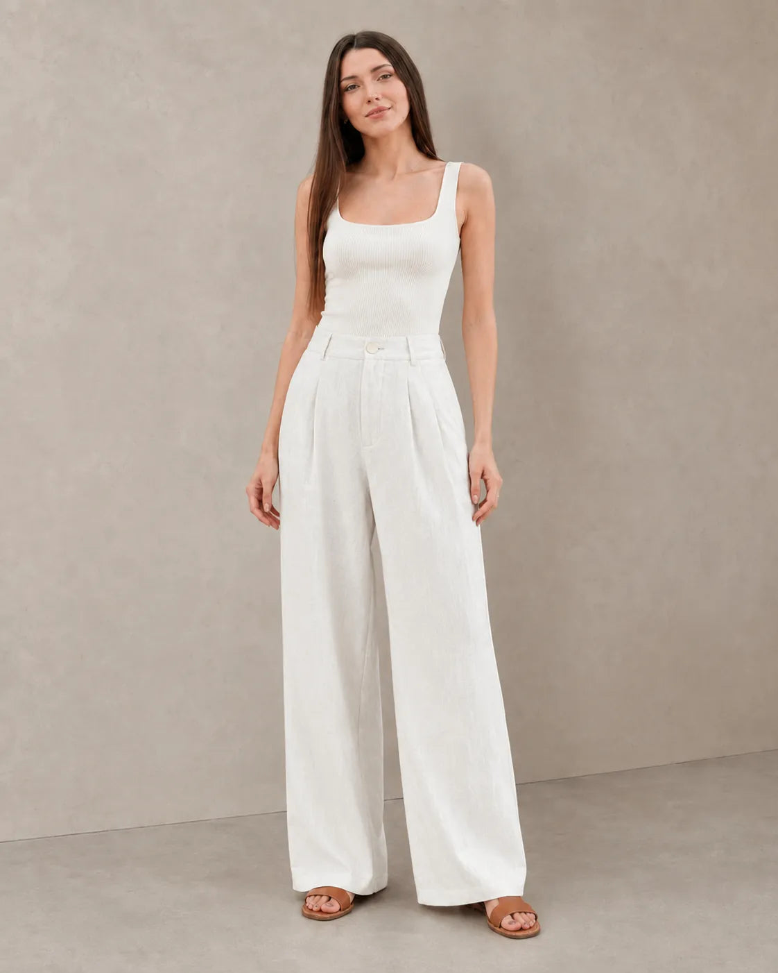 Close-up front view of model in white wide-leg summer trousers in a cotton-linen-polyester blend with a pleated high waist.