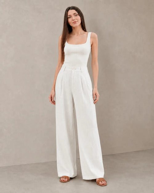 Close-up front view of model in white wide-leg summer trousers in a cotton-linen-polyester blend with a pleated high waist.