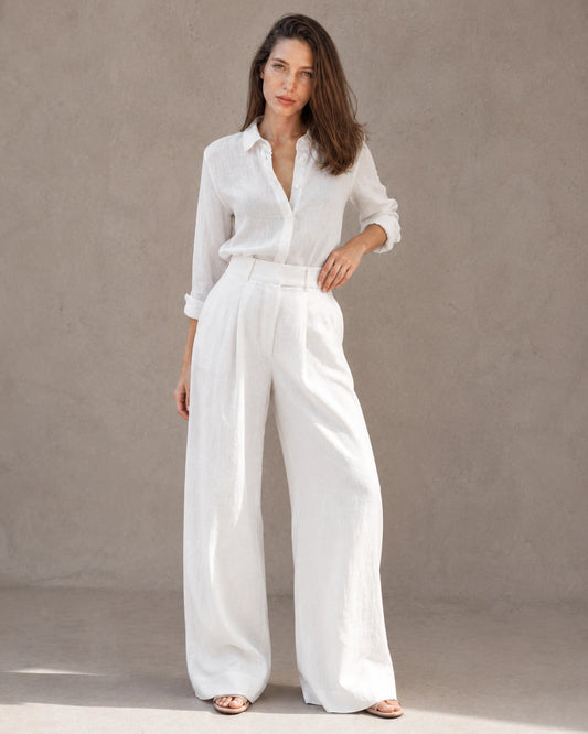 Model draagt een wijde broek dames in witte katoen-linnenmix met hoge elastische taille, gestyled met een bijpassend wit linnen overhemd, vooraanzicht.