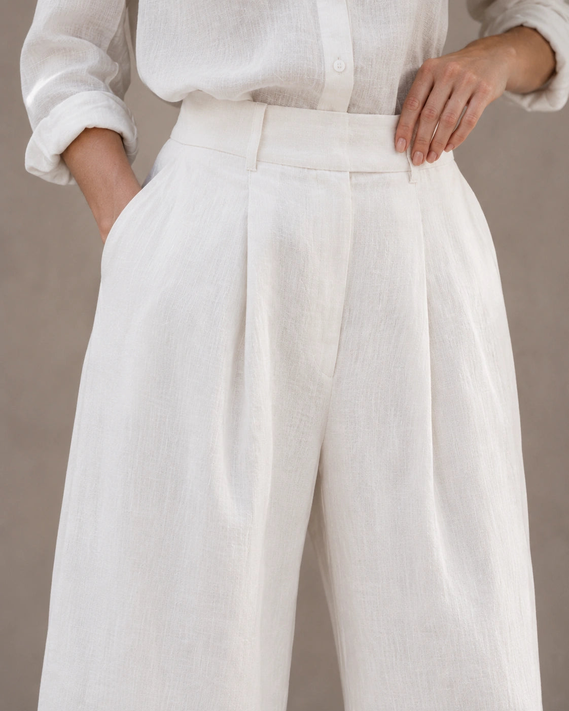 Close-up van de hoge, geplooide taille en voorzak van een wijde broek dames in witte katoen-linnenmix.