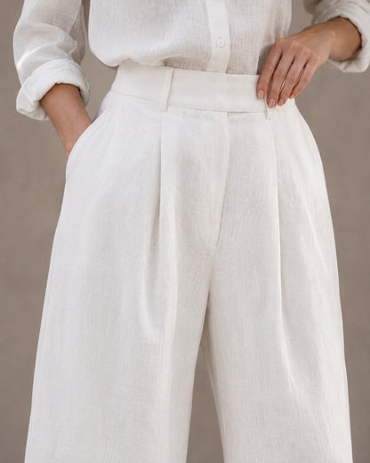 Close-up van de hoge, geplooide taille en voorzak van een wijde broek dames in witte katoen-linnenmix.