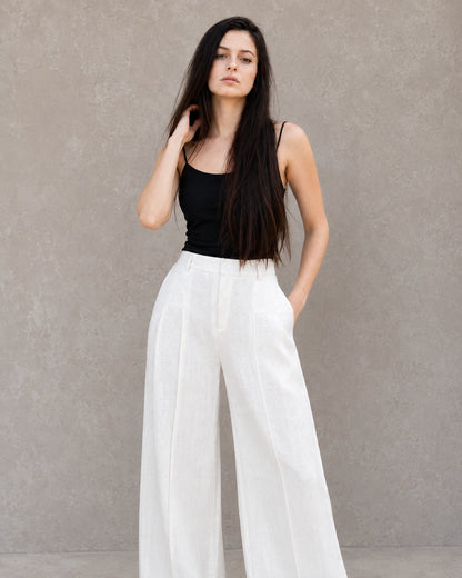 Close-up vooraanzicht van model in een witte wijde broek dames in katoen-linnenmix, hand rustend op de heup.