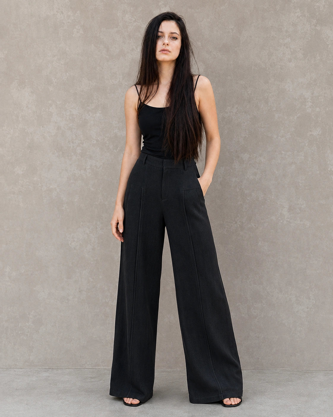 Model draagt een zwarte wijde broek dames in katoen-linnenmix met geplooide hoge taille, gestyled met een zwart hemdje, vooraanzicht.