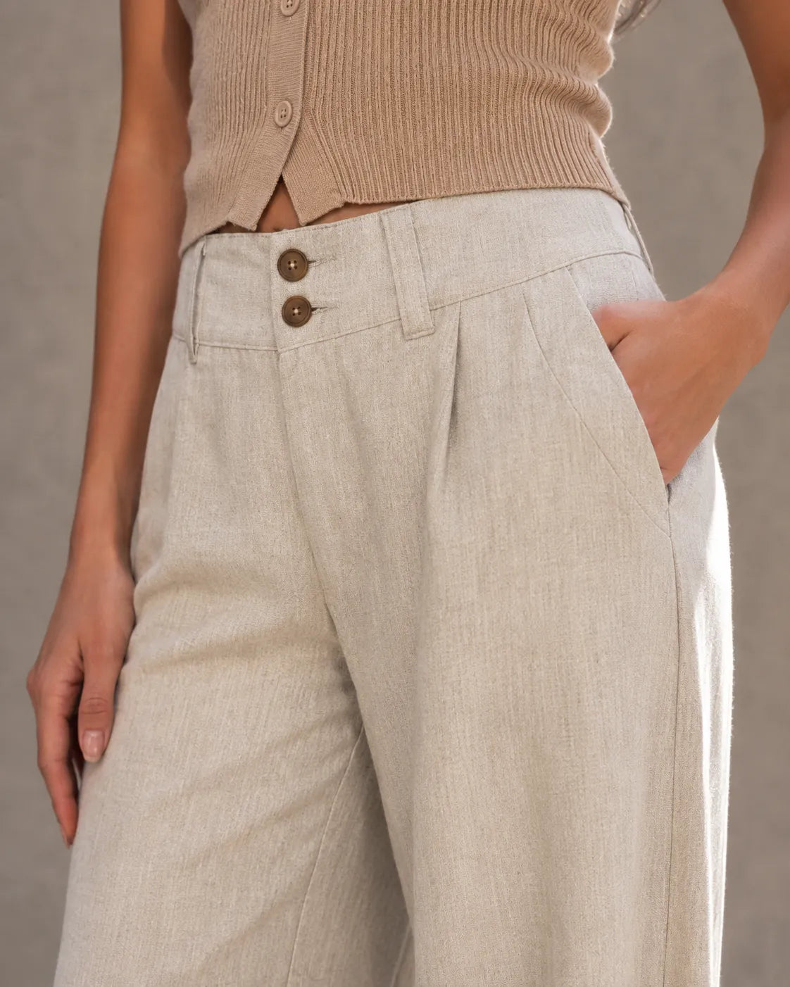Close-up van de dubbele knooptaille en zak van een enkellange linnen broek dames in gebroken wit.