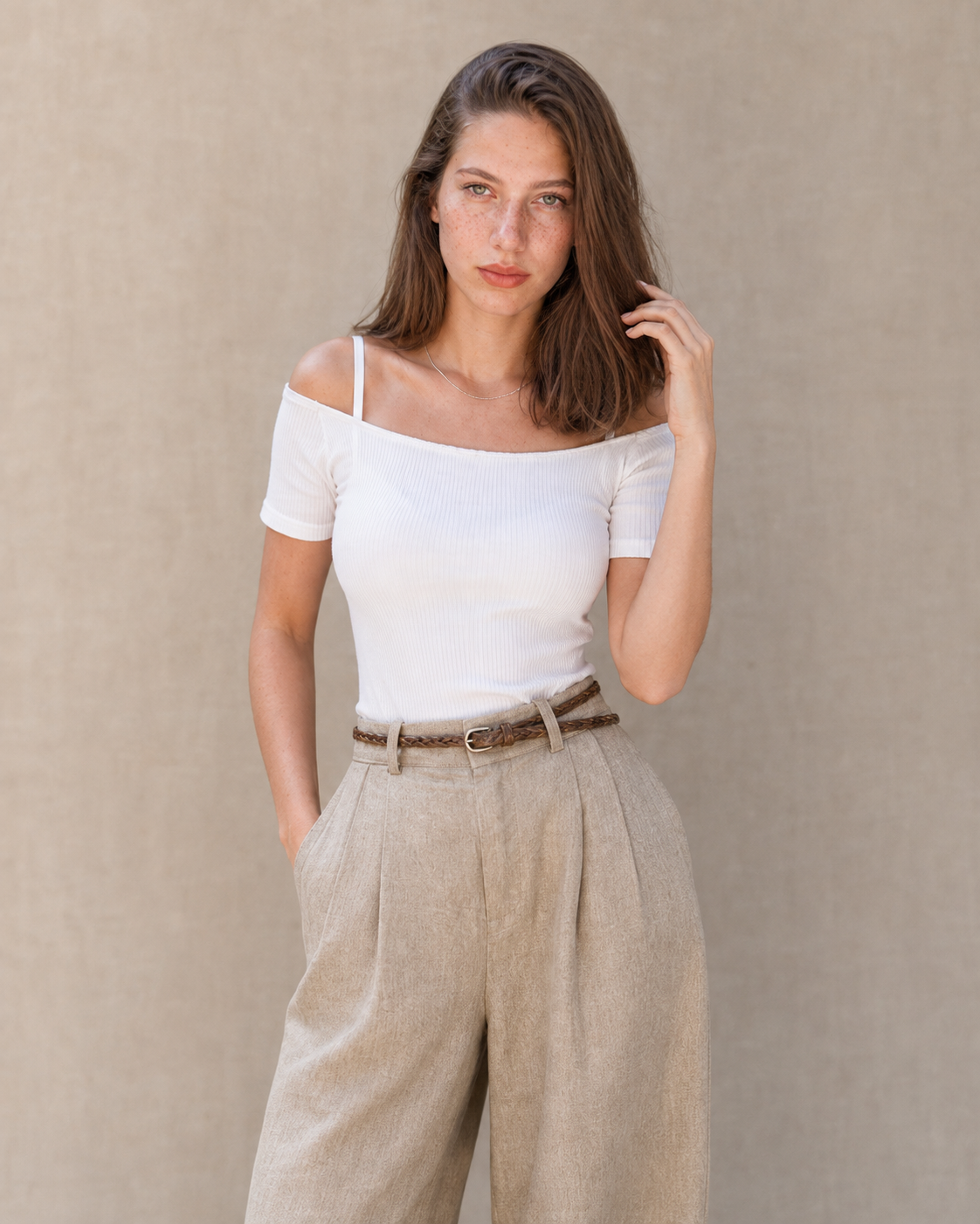 Model draagt een kaki linnen broek dames met rechte pijp en hoge taille, gestyled met een wit topje en gevlochten riem, vooraanzicht.