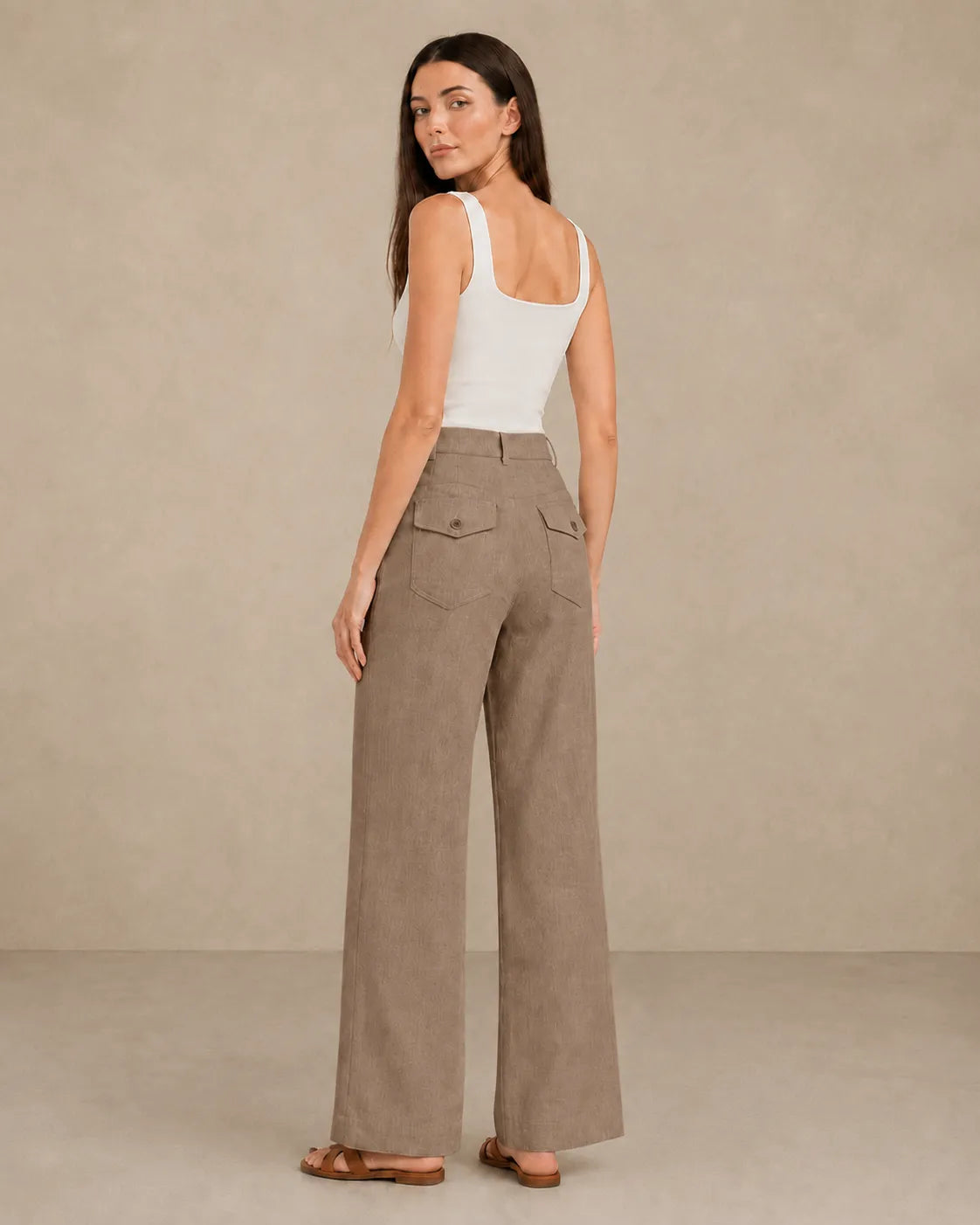 Back view of model wearing latte-coloured linen wide-leg trousers with flap patch pockets.