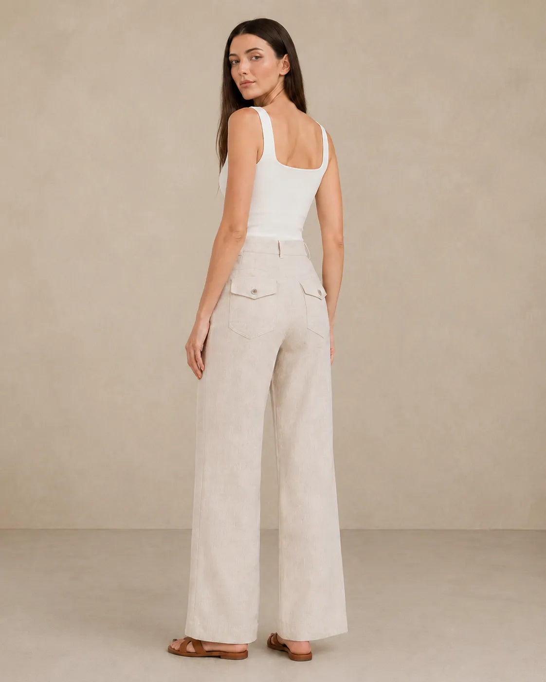 Back view of model wearing natural linen wide-leg trousers with flap patch pockets.