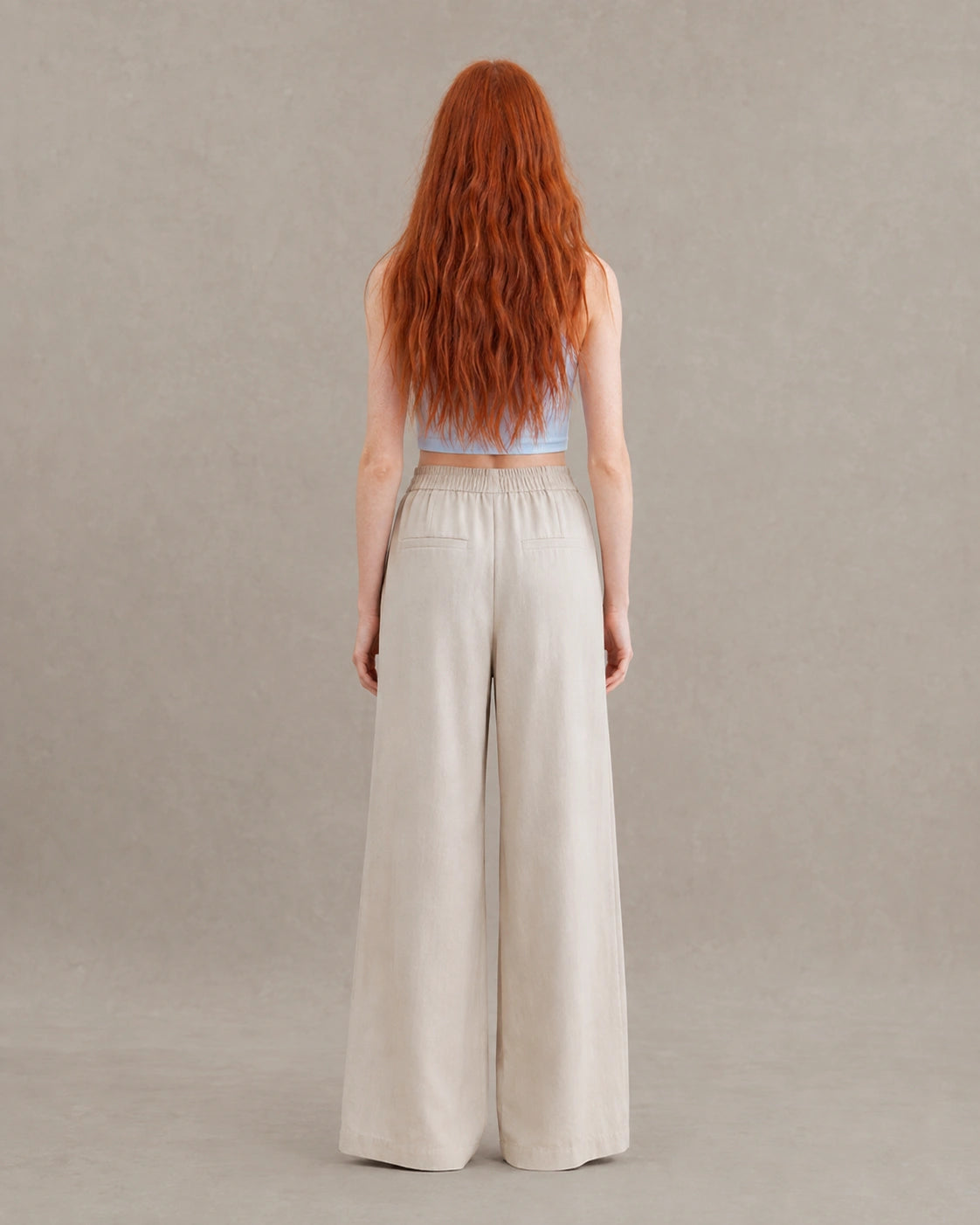 Achteraanzicht van model in een abrikooskleurige gedrapeerde linnen broek dames in linnen-polyestermix met elastische taille en steekzakken.