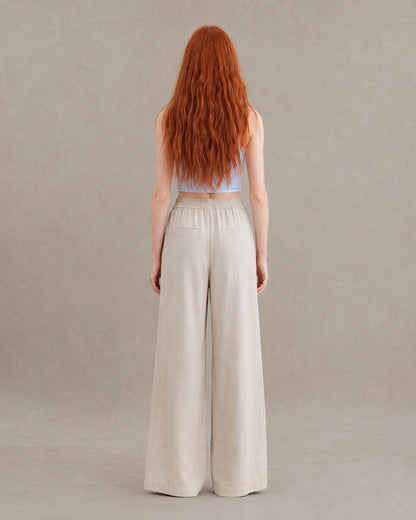 Achteraanzicht van model in een abrikooskleurige gedrapeerde linnen broek dames in linnen-polyestermix met elastische taille en steekzakken.