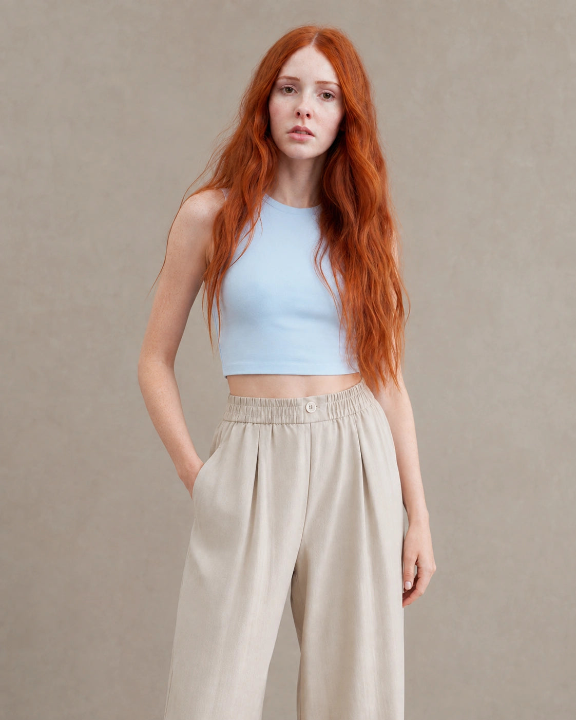 Close-up vooraanzicht van model in een abrikooskleurige gedrapeerde linnen broek dames in linnen-polyestermix met handen in de zakken.