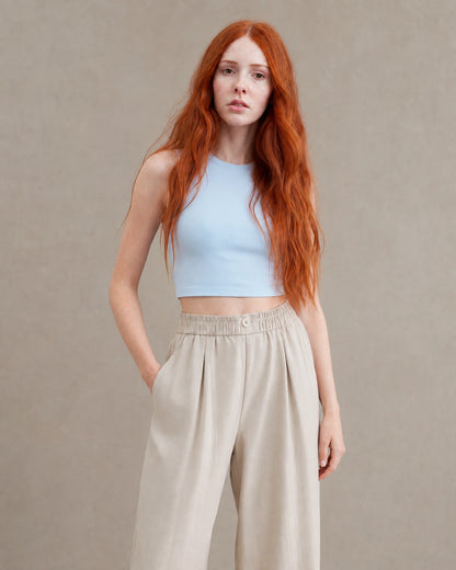 Close-up vooraanzicht van model in een abrikooskleurige gedrapeerde linnen broek dames in linnen-polyestermix met handen in de zakken.