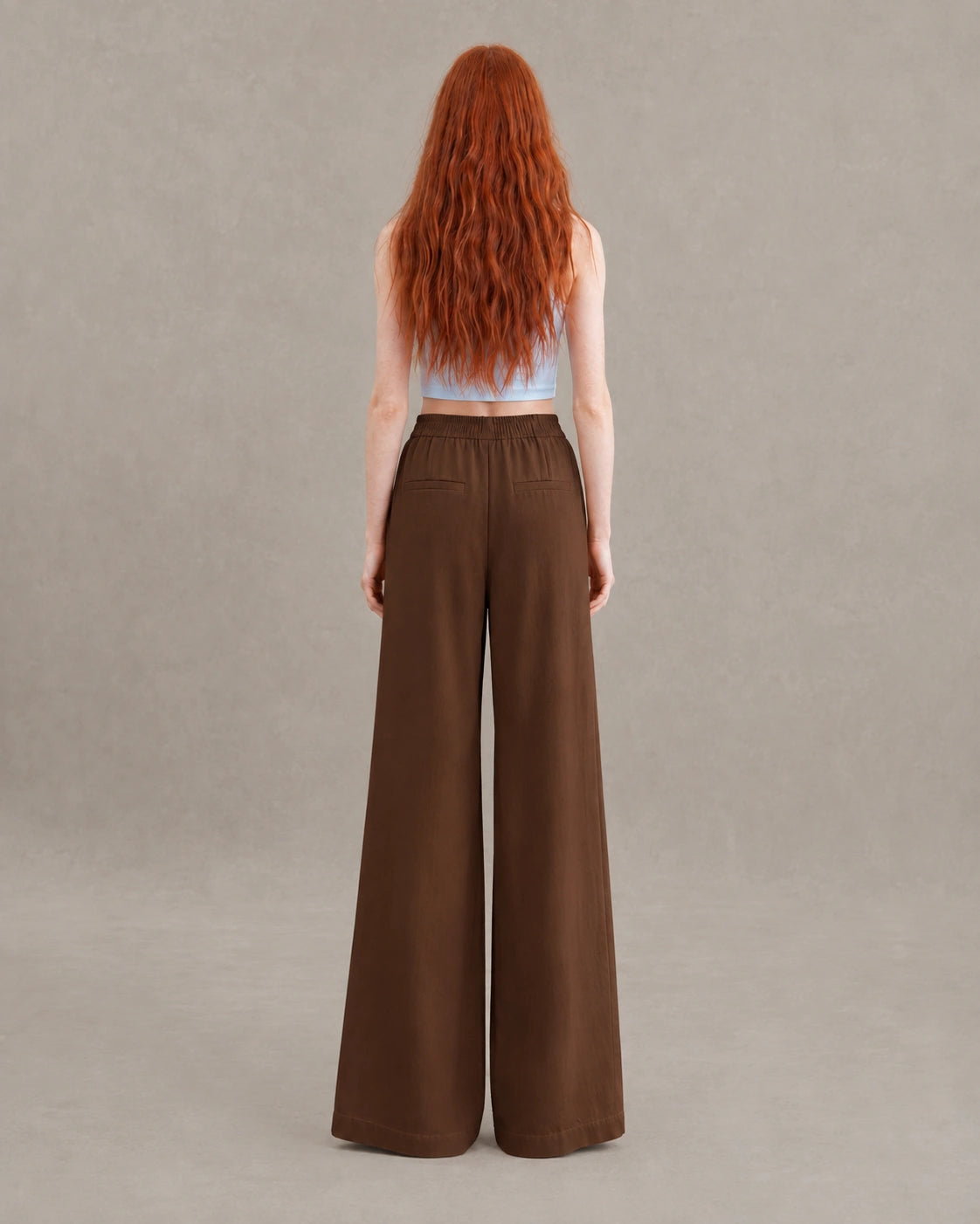 Achteraanzicht van model in een bruine gedrapeerde linnen broek dames in linnen-polyestermix met elastische taille en steekzakken.
