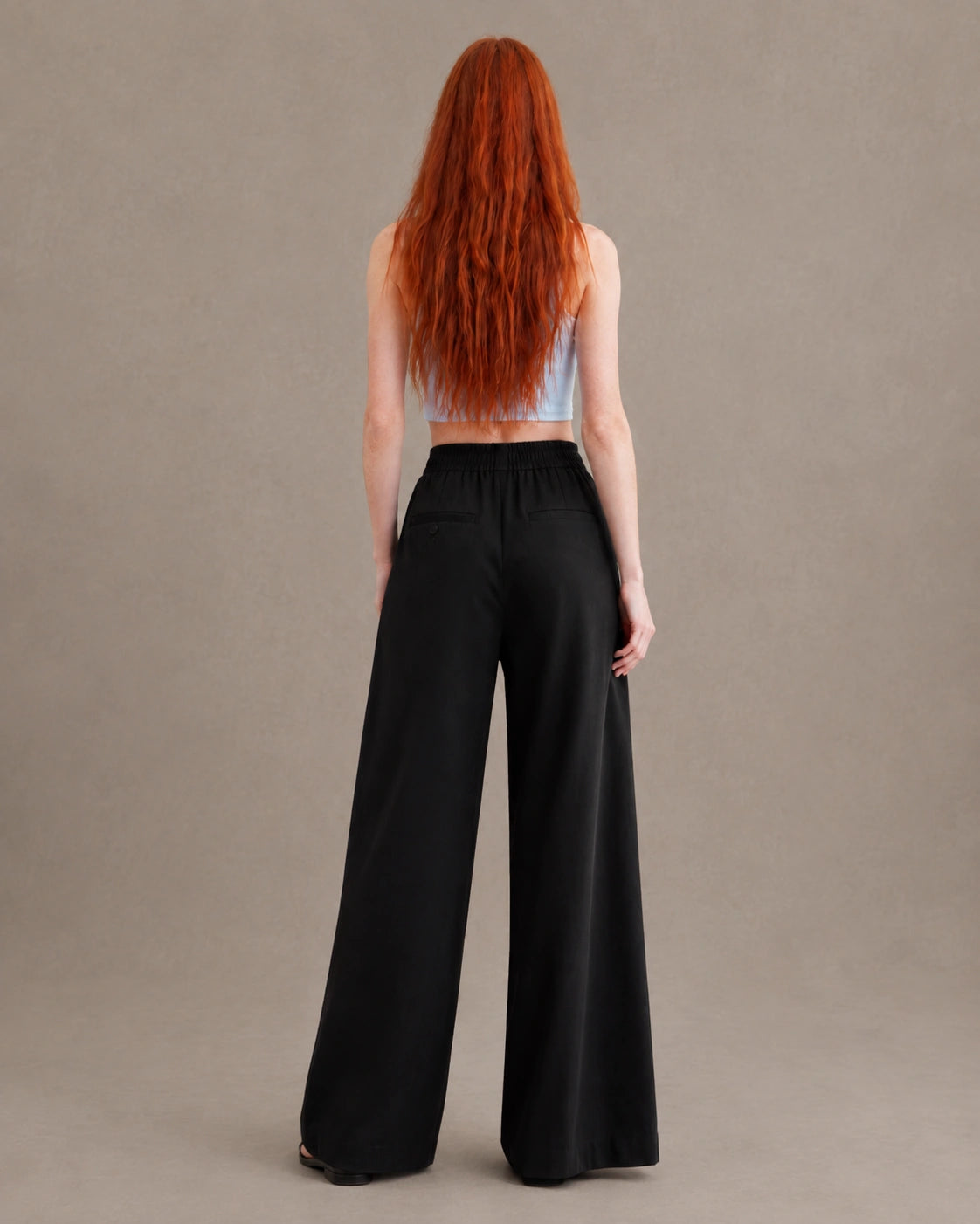 Achteraanzicht van model in een zwarte gedrapeerde linnen broek dames in linnen-polyestermix met elastische taille en steekzakken.