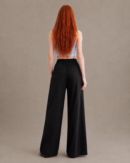 Achteraanzicht van model in een zwarte gedrapeerde linnen broek dames in linnen-polyestermix met elastische taille en steekzakken.