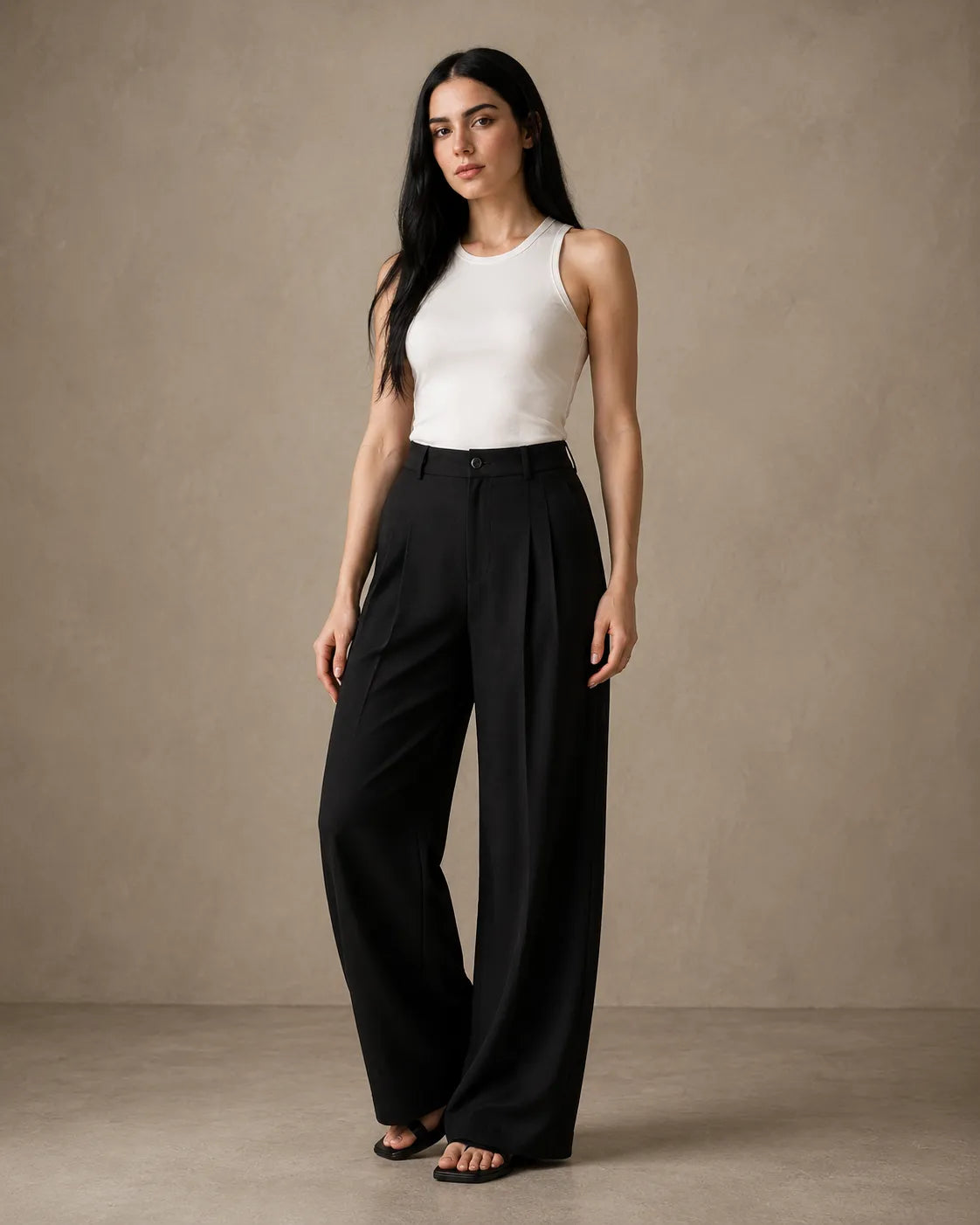 Model wearing black wide-leg trousers in a linen-tencel-viscose blend with a pleated high waist, styled with a white tank top, front view.