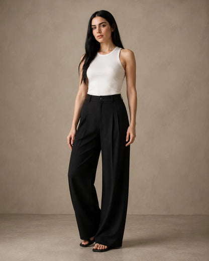 Model wearing black wide-leg trousers in a linen-tencel-viscose blend with a pleated high waist, styled with a white tank top, front view.
