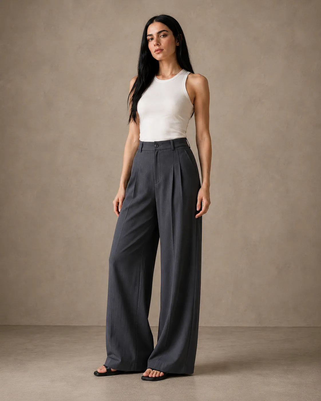 Model wearing dark grey wide-leg trousers in a linen-tencel-viscose blend with a pleated high waist, styled with a white tank top, front view.