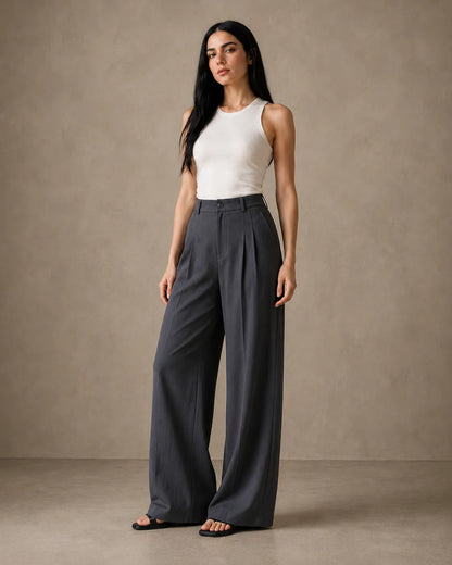 Model wearing dark grey wide-leg trousers in a linen-tencel-viscose blend with a pleated high waist, styled with a white tank top, front view.