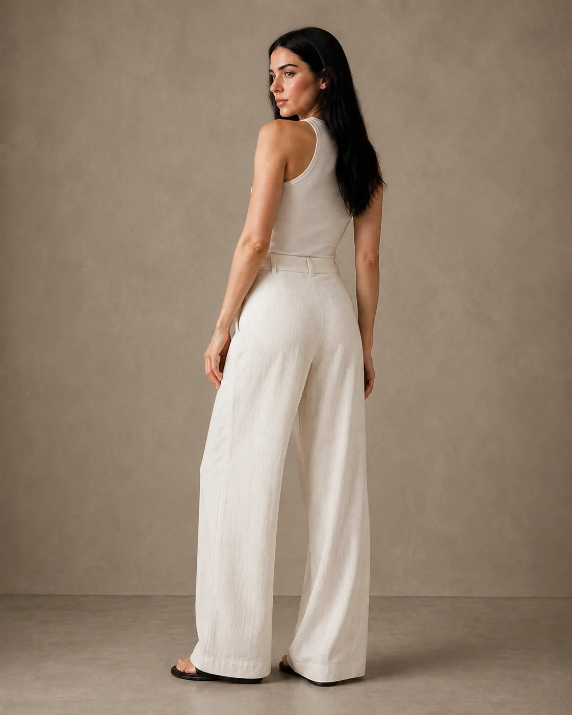 Three-quarter back view of model wearing oatmeal white wide-leg trousers in linen-tencel-viscose blend.
