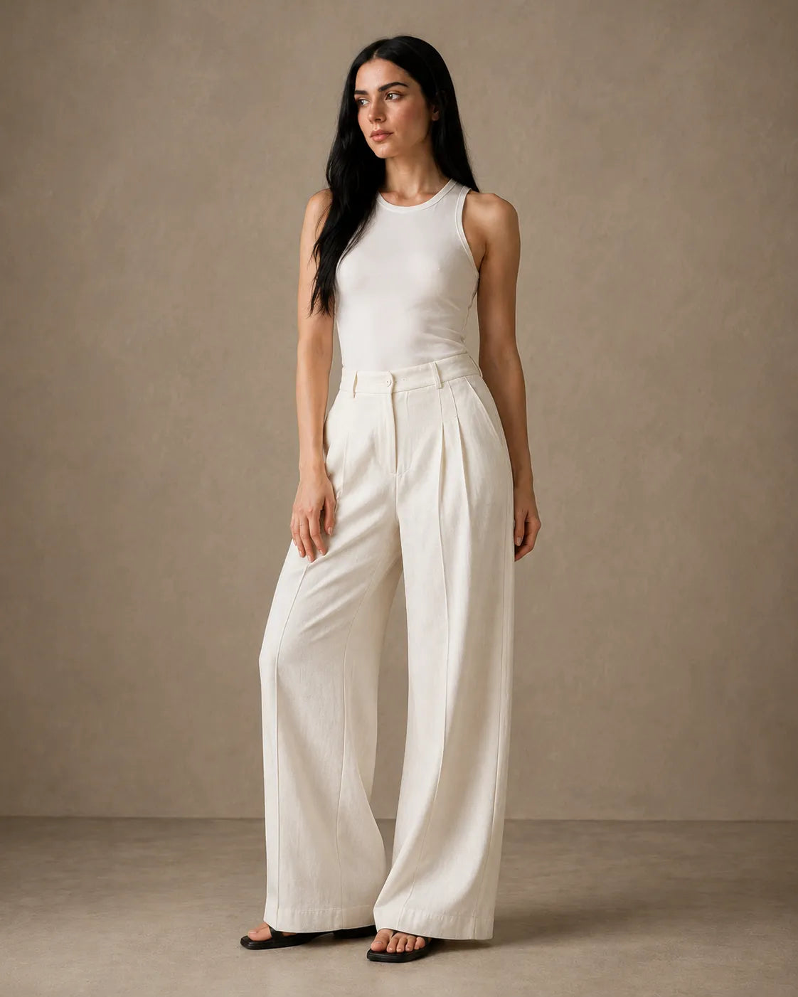 Model wearing oatmeal white wide-leg trousers in a linen-tencel-viscose blend with a pleated high waist, styled with a white tank top, front view.