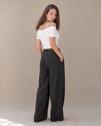 Achteraanzicht van model in een zwarte linnen broek dames met rechte pijp, hoge taille en gevlochten riem.
