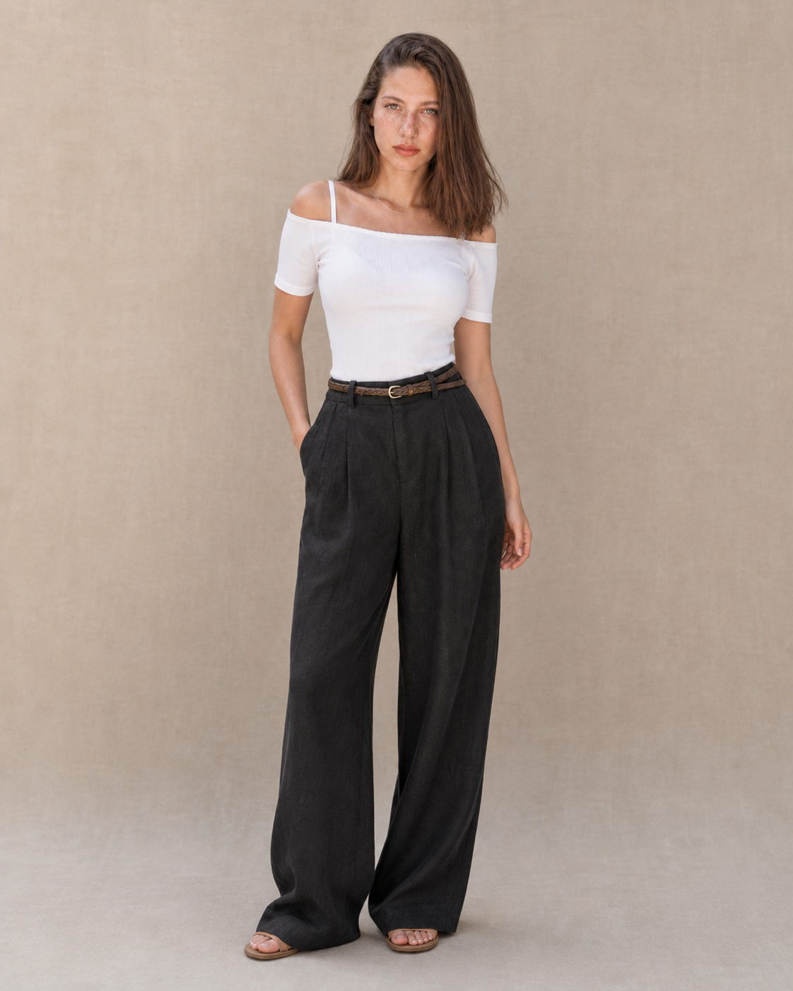 Model draagt een zwarte linnen broek dames met rechte pijp en hoge taille, gestyled met een wit topje en gevlochten riem, vooraanzicht.