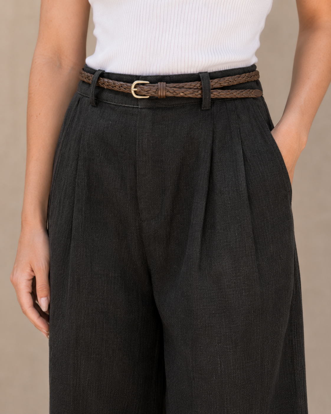 Close-up van de hoge, geplooide taille en gevlochten riem van een zwarte linnen broek dames met rechte pijp.