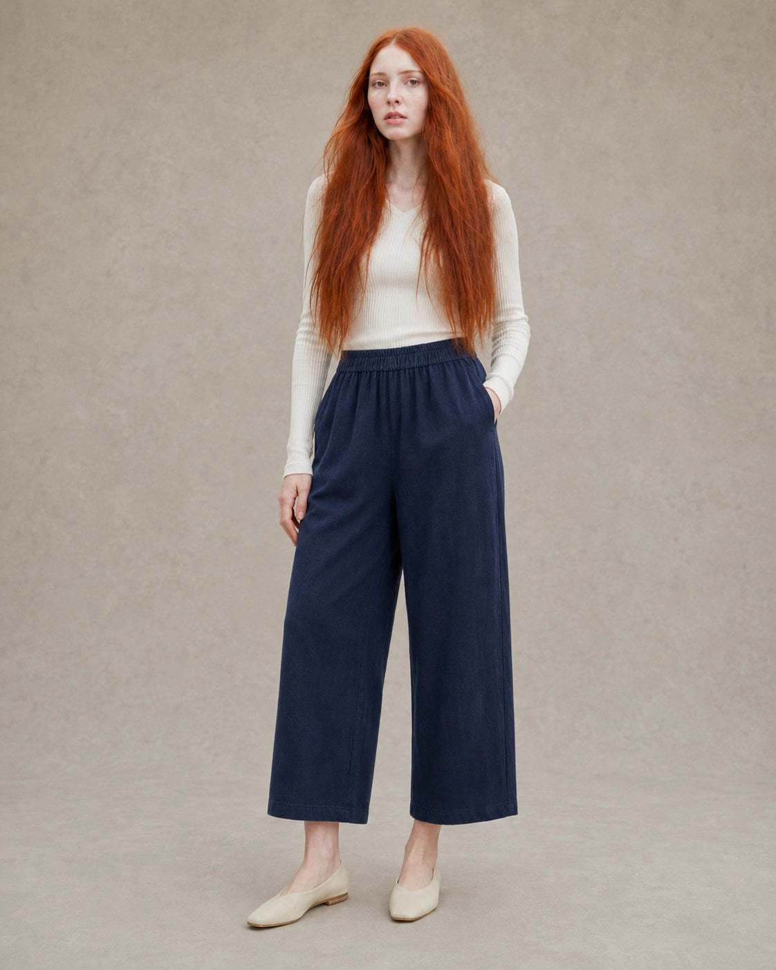 Model draagt een ingekorte wijde broek dames in donkerblauwe tencel-linnenmix met elastische taille, gestyled met een crème geribbelde top, vooraanzicht.