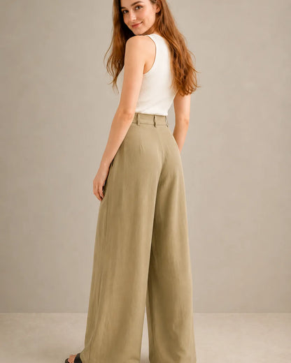 Three-quarter back view of a model looking over her shoulder, wearing khaki-toned wide-leg trousers in a tencel-linen blend with a draped finish, styled with a white tank top.