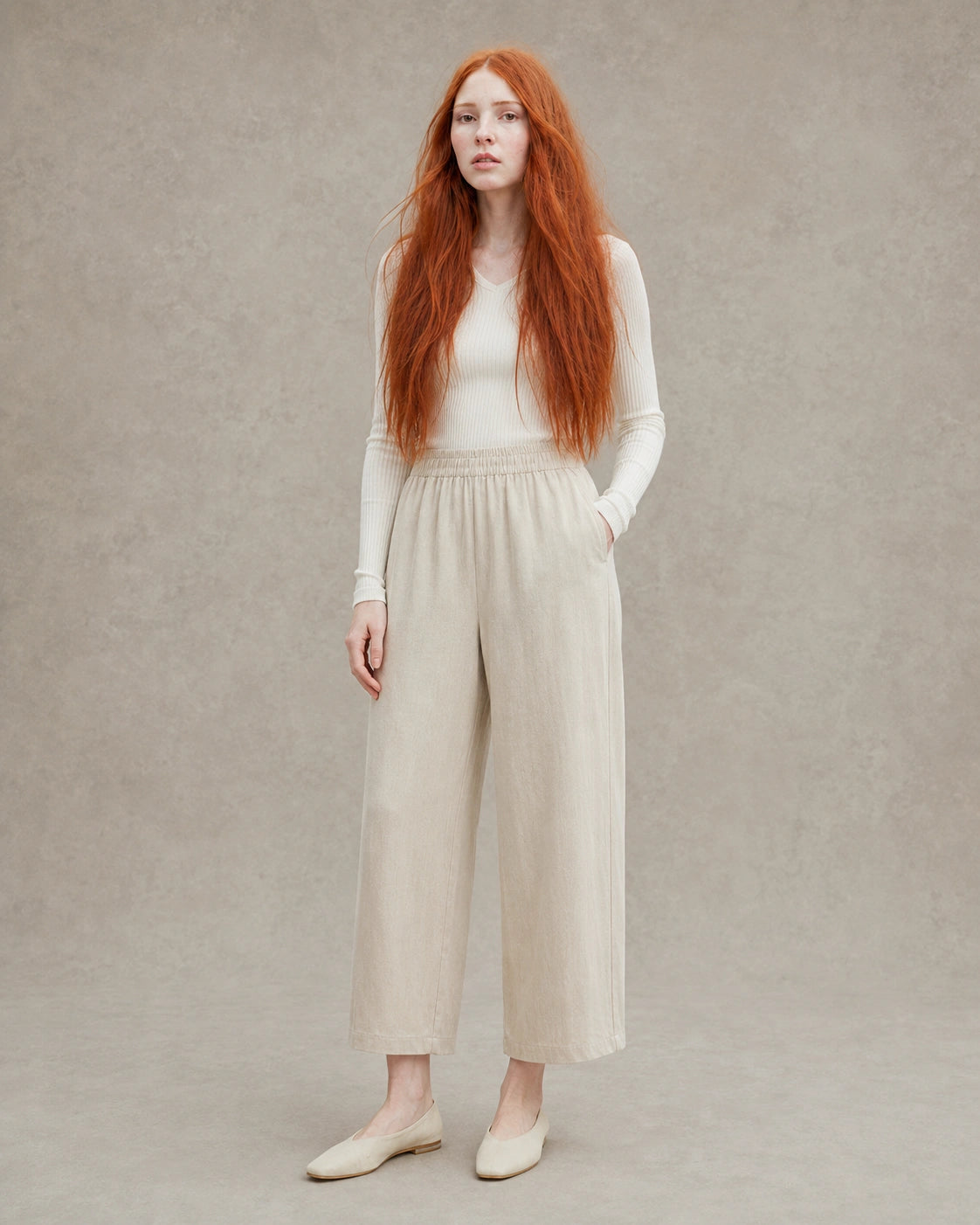 Model draagt een ingekorte wijde broek dames in kaki tencel-linnenmix met elastische taille, gestyled met een crème geribbelde top, vooraanzicht.