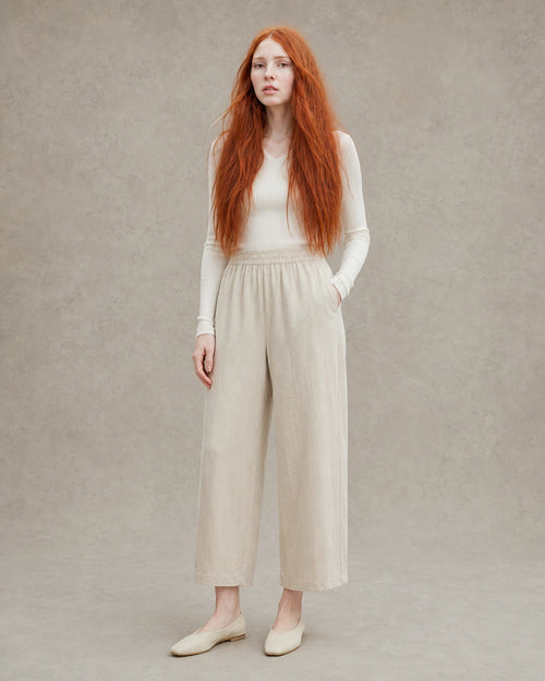 Model draagt een ingekorte wijde broek dames in kaki tencel-linnenmix met elastische taille, gestyled met een crème geribbelde top, vooraanzicht.