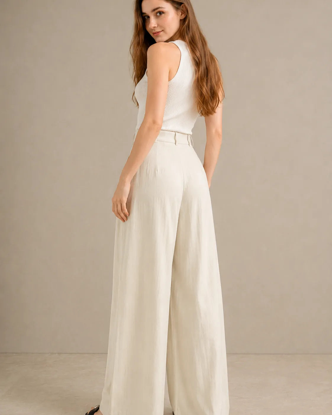 Back view of model wearing white wide-leg trousers in a tencel-linen blend with a draped finish.