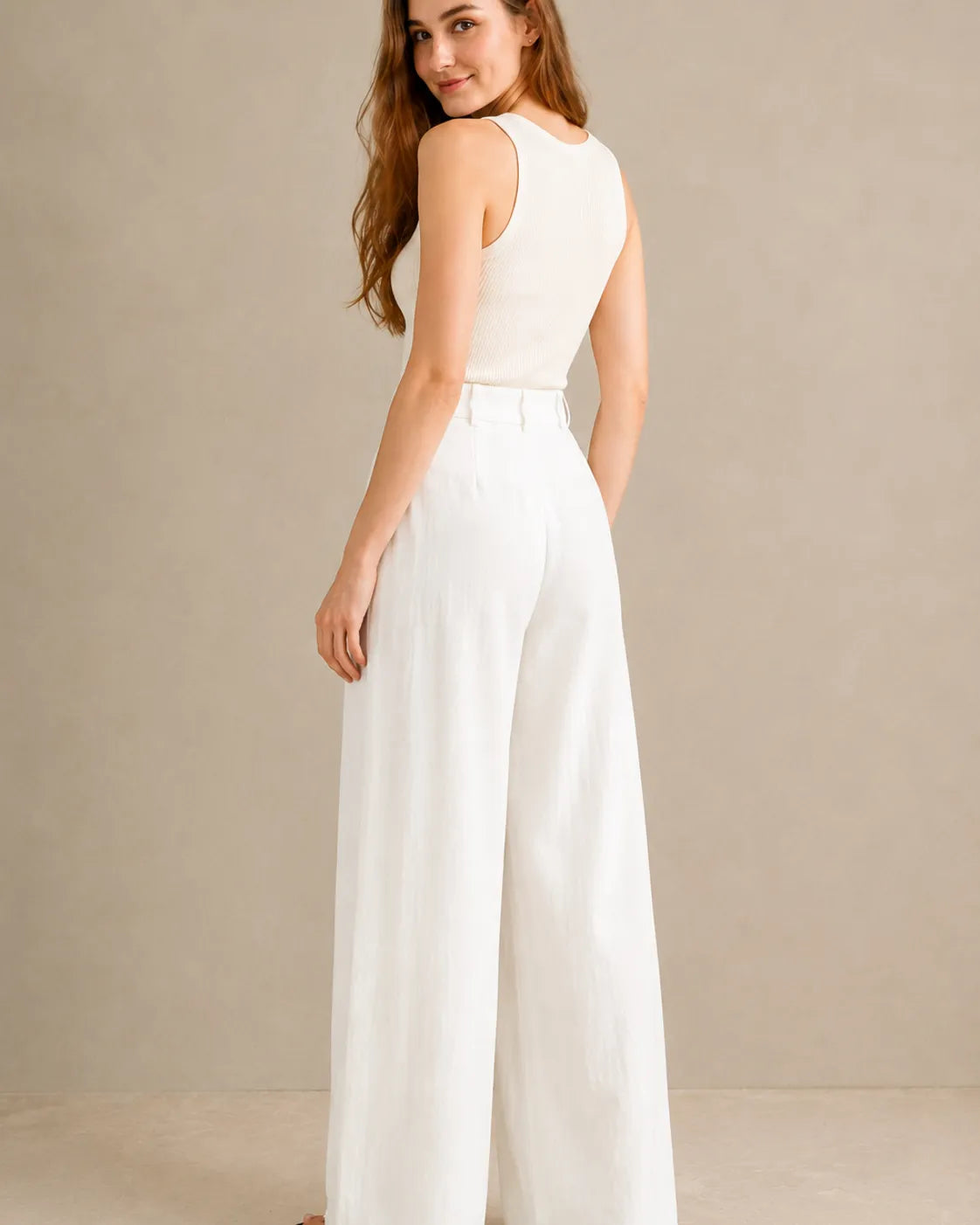 Three-quarter back view of model wearing white wide-leg trousers in a tencel-linen blend with a draped finish.
