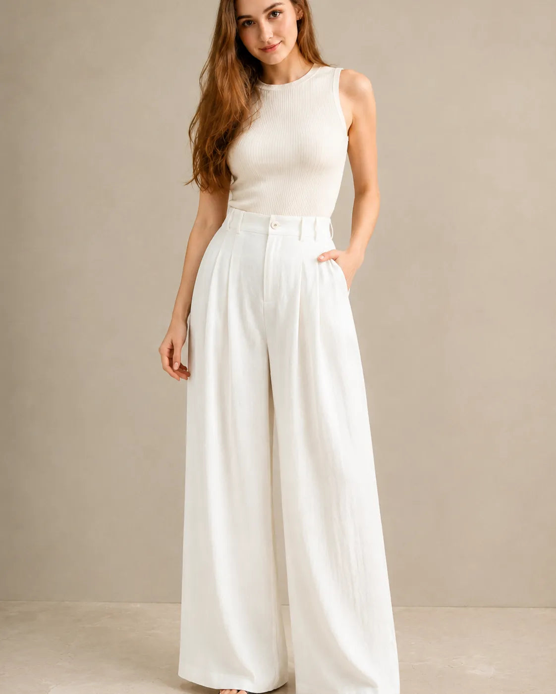 Model wearing white wide-leg trousers in a tencel-linen blend with a draped finish and pleated high waist, styled with an ivory ribbed tank top, front view.